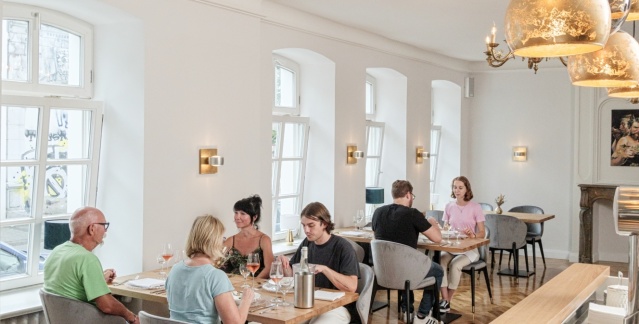 Innenansicht der Räumlichkeit des Restaurants Handelshof mit Gästen an zwei Tischen und goldenen Lampen 