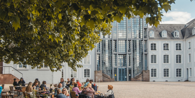Außenansicht Café am Schloss: Tische unter großen Baum mit Blick auf das Saarbrücker Schloss