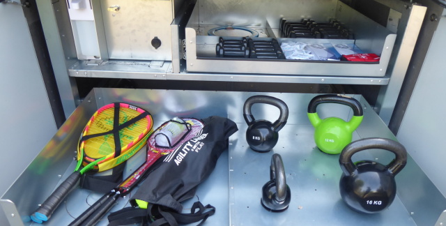 Sportbox Schublade mit vier Gewichten von vier bis 16 Kilo, daneben Schläger.