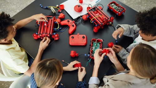 Open Lab Kinder bauen mit einem Bausatz und Platinen, Kabeln, Leuchtdioden und Schaltern ein kleines, rotes Fahrzeug zusammen